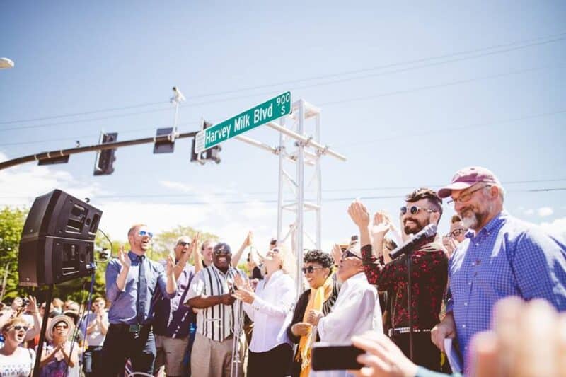 Clapping happy people under a street sign: Harvey Milk Blvd