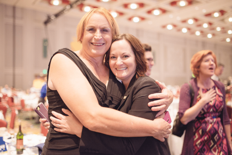 Two women hugging, looking at camera