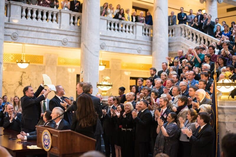 A large crowd gathers inside the capitol, clapping as a lifts up a document to them.