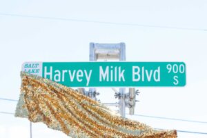 Street sign that reads 'Harvey Milk Blvd' as a gold sequin fabric unveils it.