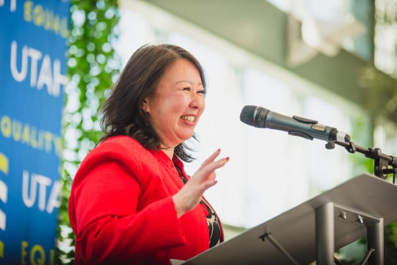 A woman in a bright red suit smiles behind a speaker's podium