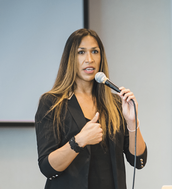 A woman wearing a black suit speaks into a microphone