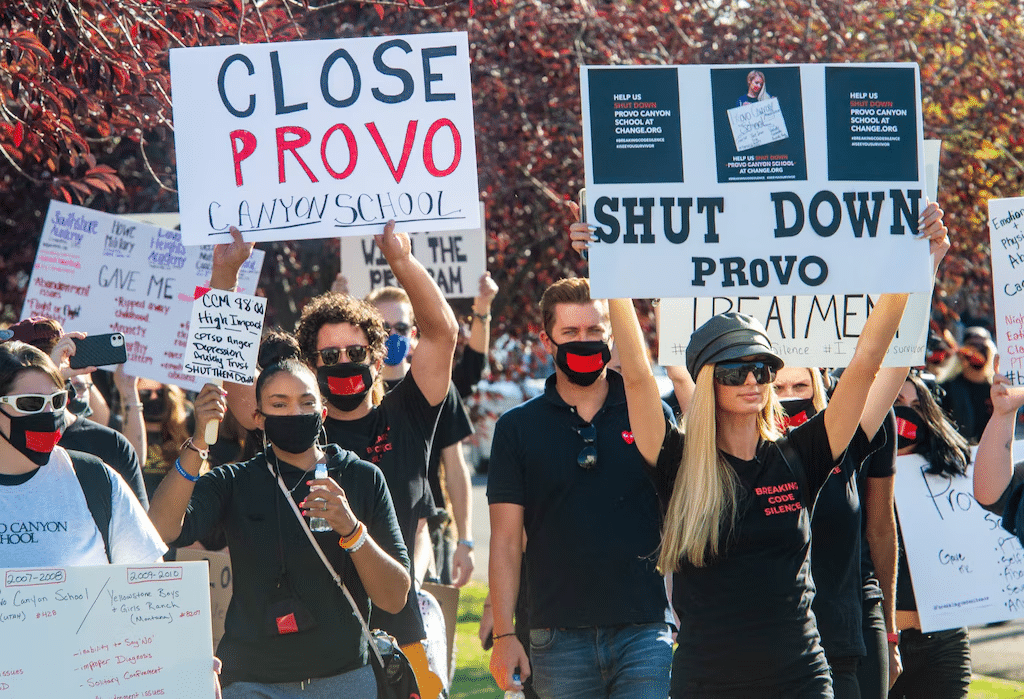 A group of protestors wearing face masks hold signs with the text 'CLOSE PROVO CANYON SCHOOL' 'SHUT DOWN PROVO'