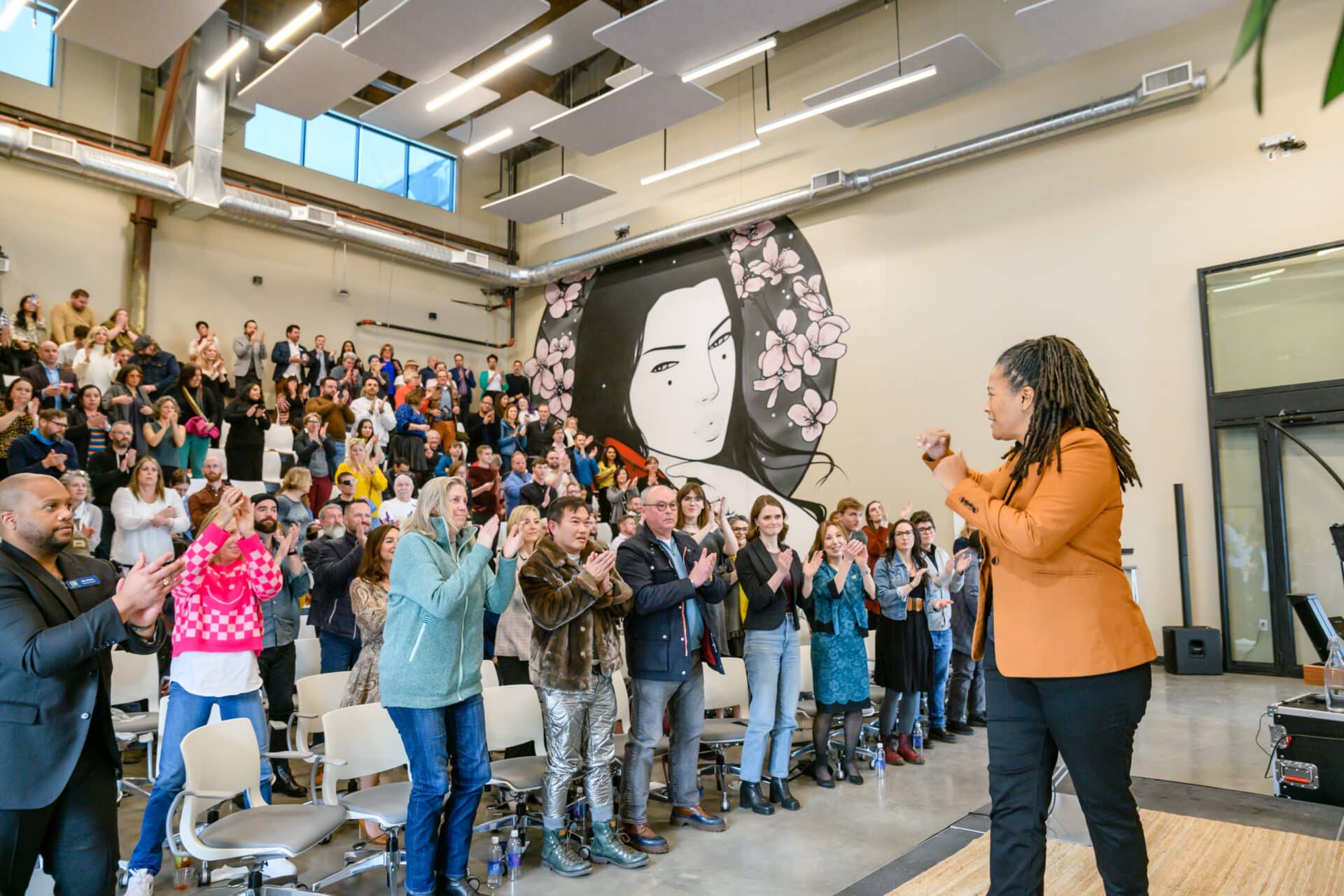 Woman stands on a stage faces a crowd that is standing a clapping.