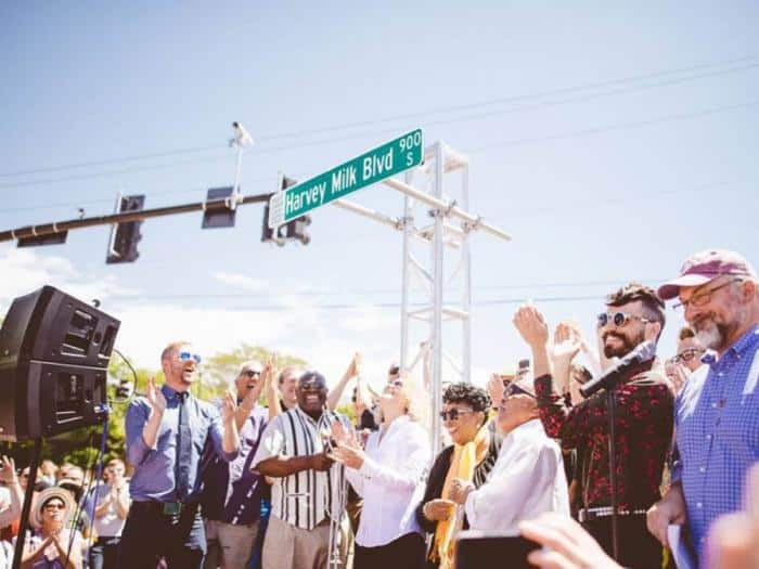 Group cheers under a street sign named 'Harvey Milk Blvd'